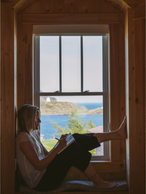 A woman seated at a window overlooking a lighthouse in Trinity