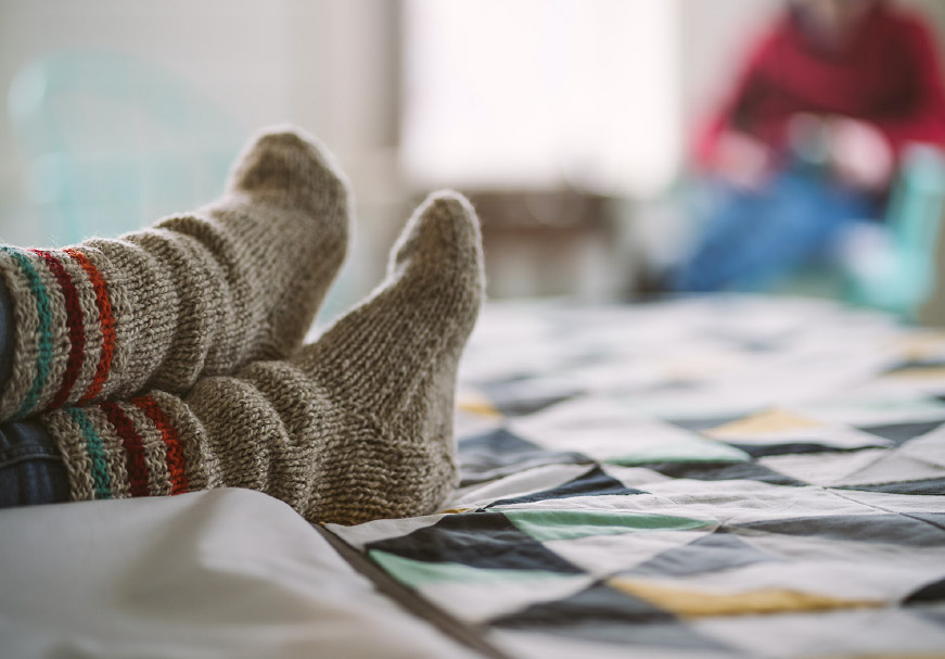 Person’s feet in cozy lounge socks, crossed on a bed