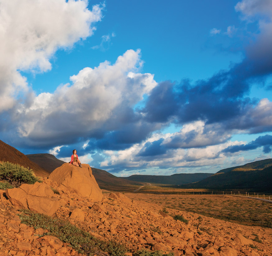 Woman sitting atop a rock in the secluded Tablelands at Gros Morne National Park