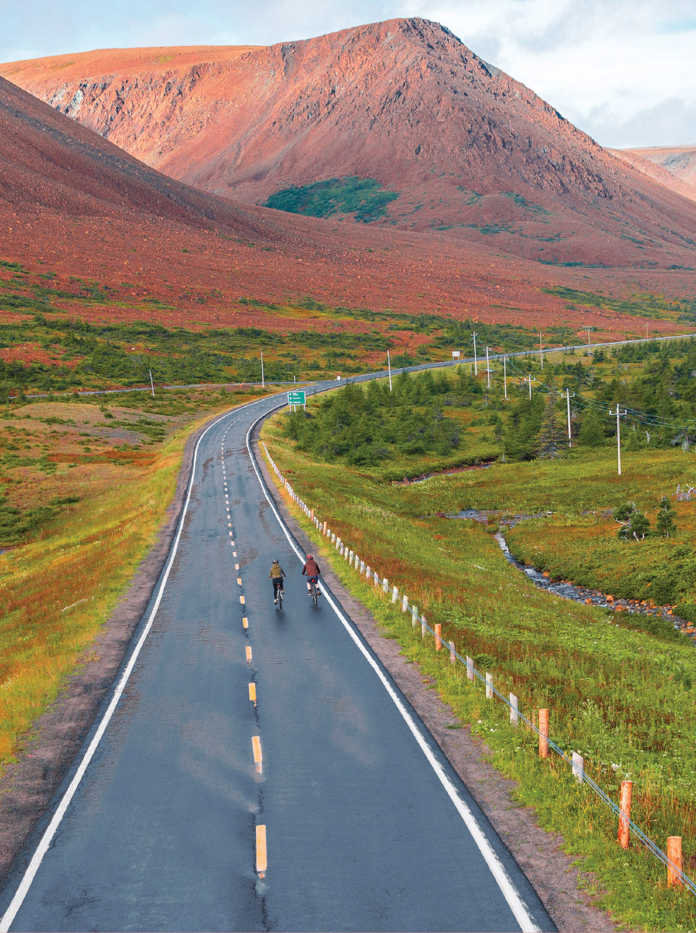 Two people biking on a long, secluded road by the Tablelands in Gros Morne National Park