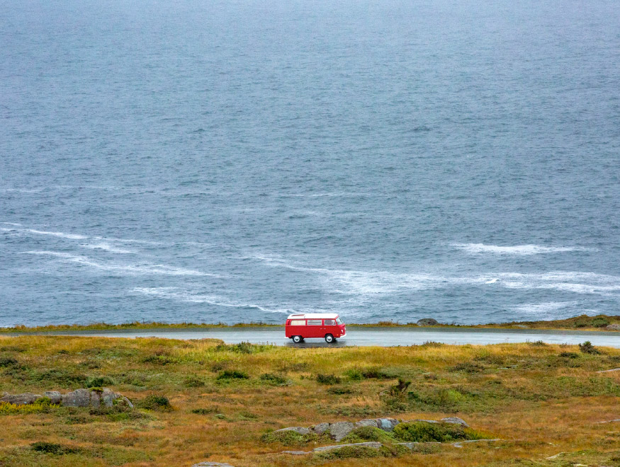 A van driving on a secluded road by an expanse of beautiful water